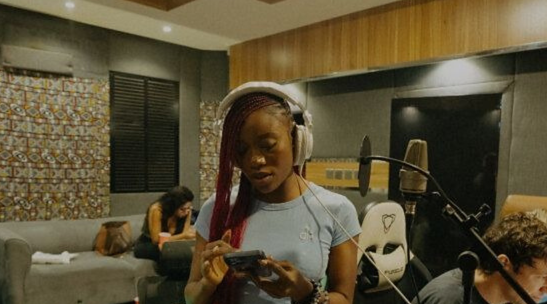 A young woman with headphones in a Lagos recording studio, a microphone and a producer at the desk beside her